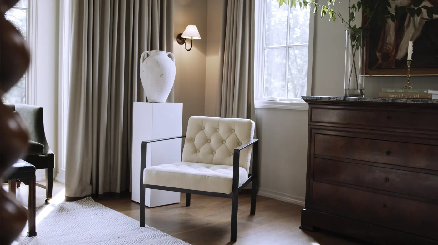 Tufted chair beside a white urn and sconce in warm afternoon light