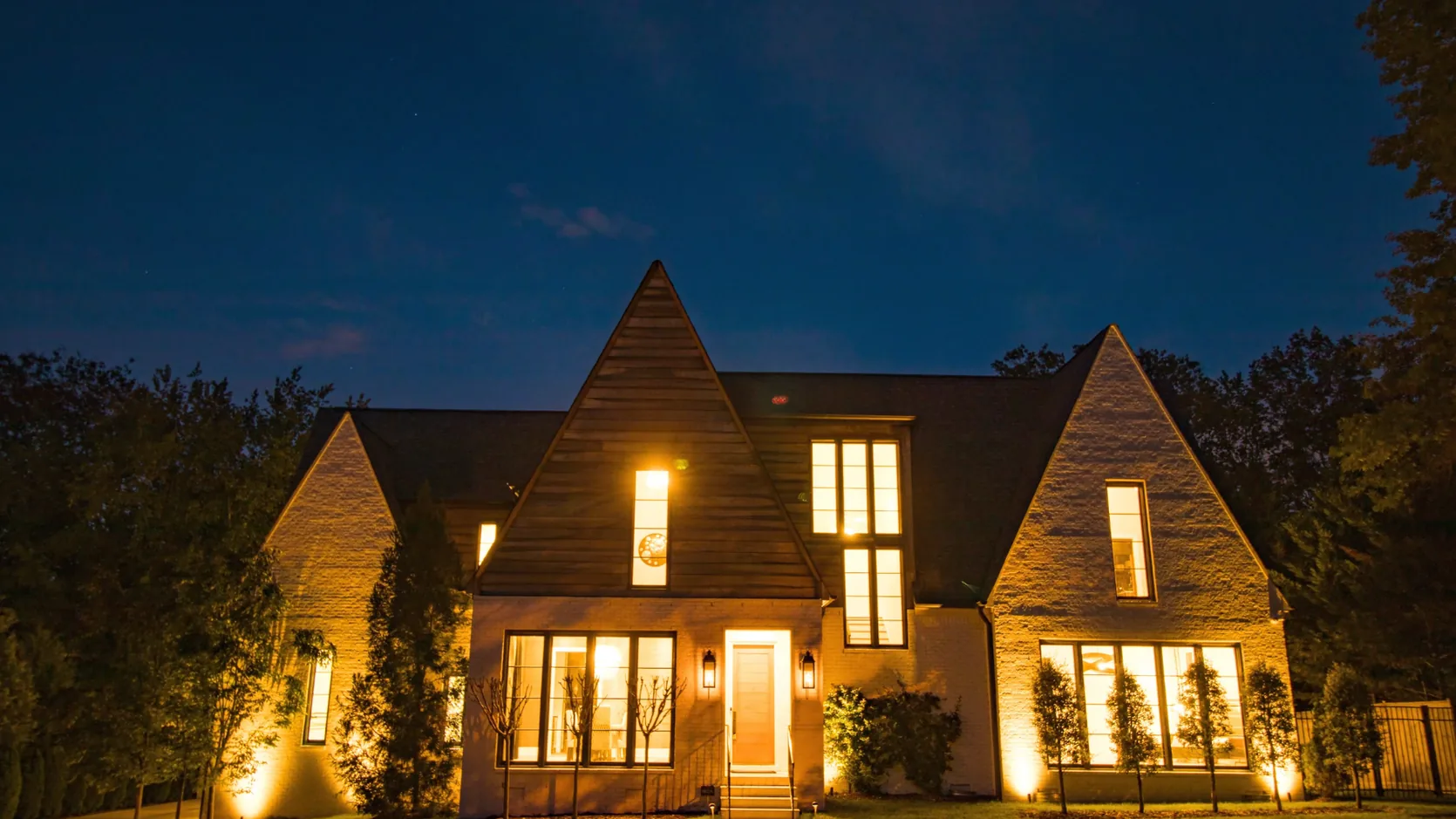 The same Nashville home at twilight with warm landscape and window lighting